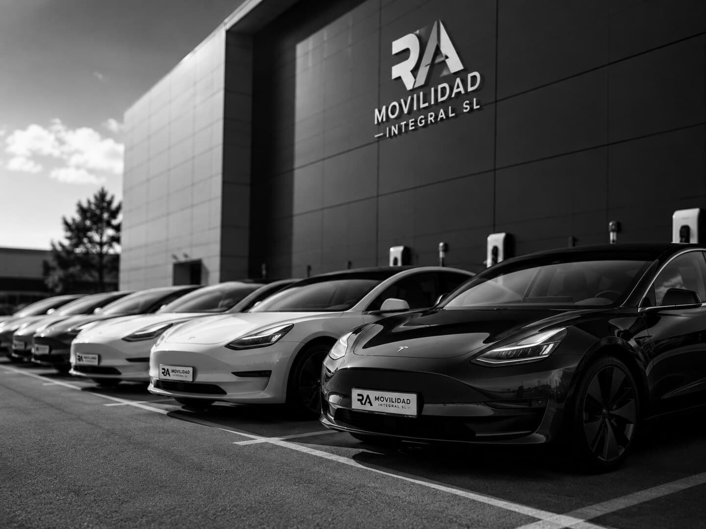 Flota de vehículos eléctricos de RA Movilidad aparcada frente a las instalaciones de la empresa